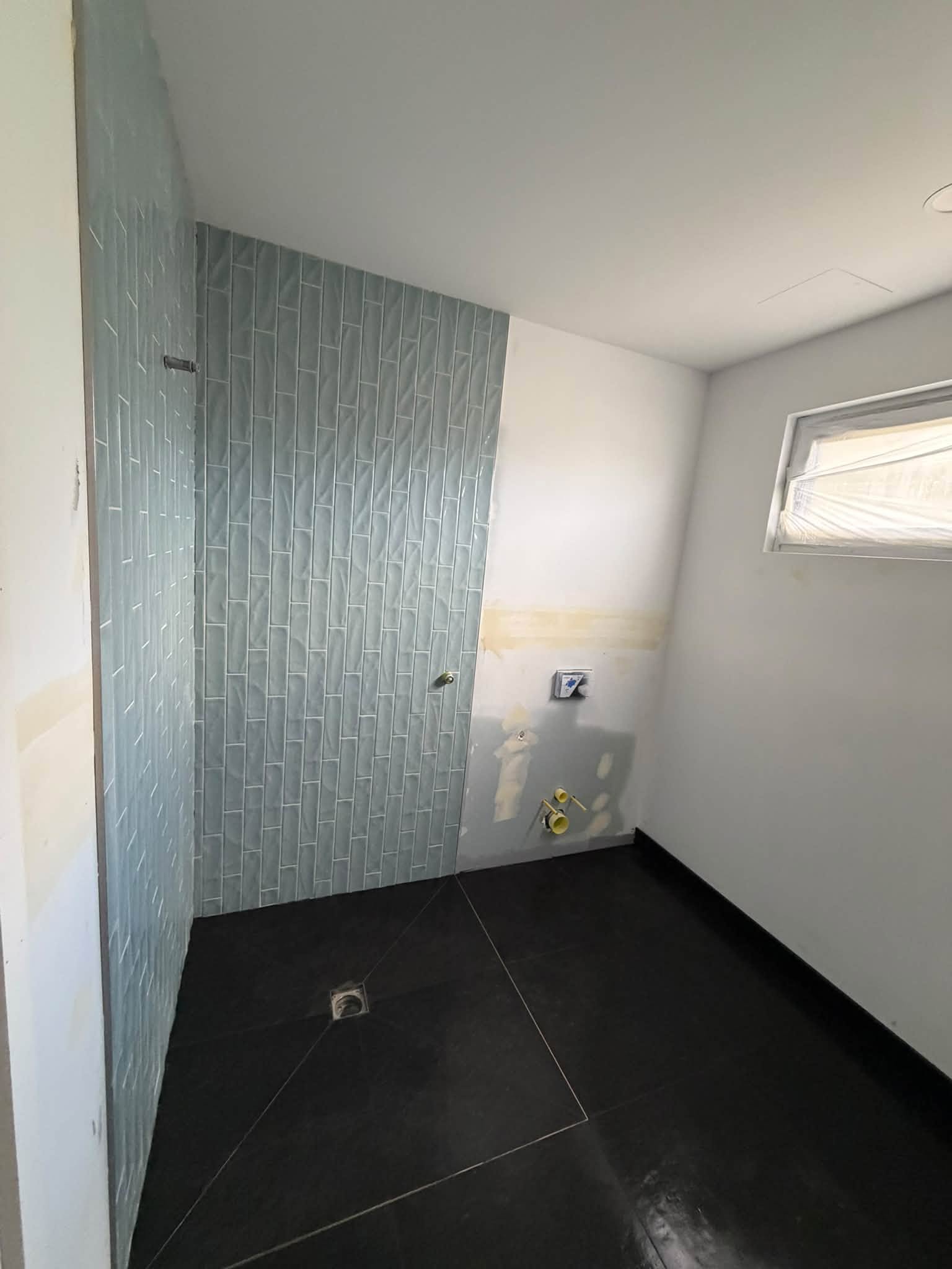 Vertical stacked sage-green feature wall tiling above a dark large-format tiled floor